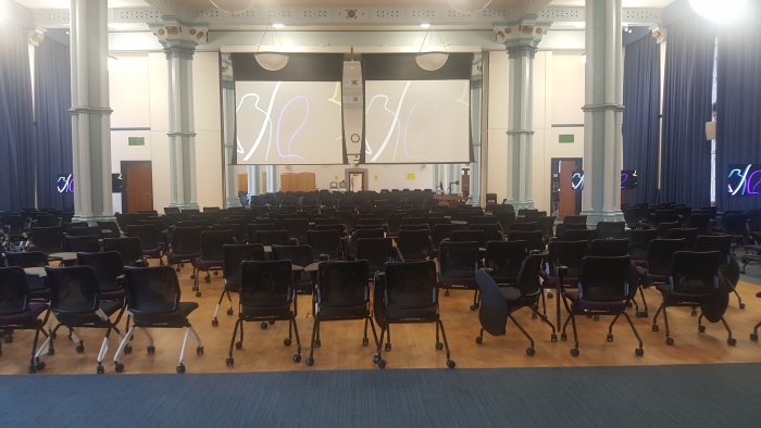 Flat floored hall with rows of tablet chairs, screens, and video monitors