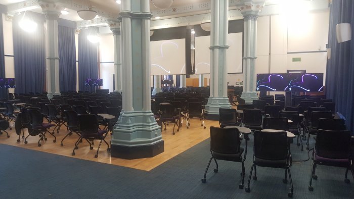 Flat floored hall with rows of tablet chairs, screens, and video monitors