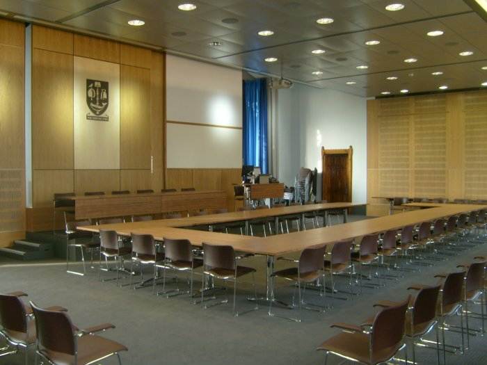 Large flat floored meeting room with tables and chairs in horseshoe set-up, raised podium, projector, and screen