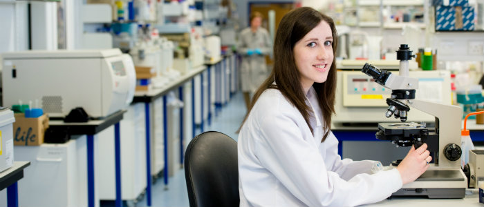 A female scientist sat in the lab using a microscope