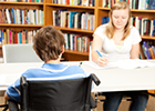 Image of a female student studying in the library, accompanied by a young man in a wheelchair