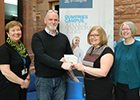 University of Glasgow colleagues Audrey Clowe (left) and Natalie Anderson (right) who organised the University of Glasgow’s Christmas Concert joined Dr Carol Hill, Head of School at the University of Glasgow in Dumfries to present Owen Fielding, Business Operations Manager from Compass Brain Injury Specialists with a cheque for £864.02. 