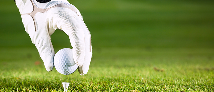 Image of a golf-gloved hand placing a ball on a golf tee. 