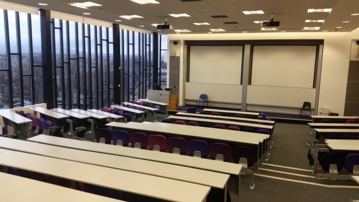 Raked lecture theatre with fixed seating, two whiteboards, screens, and projectors