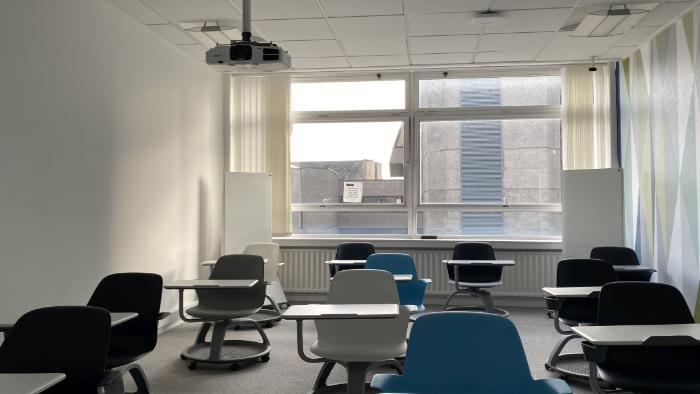 Flat floored teaching room with tablet chairs, projector, and moveable glassboards.