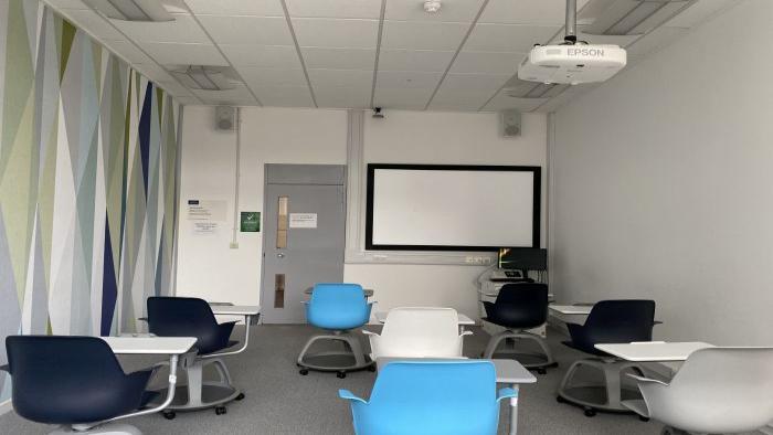 Flat floored teaching room with tablet chairs, PC, projector, and large screen.