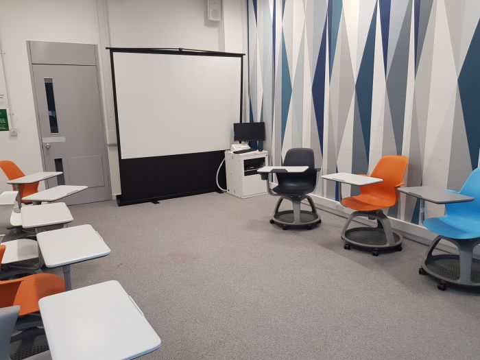 Flat floored teaching room with tablet chairs, PC, and large screen.