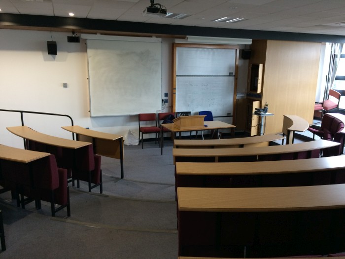 Raked lecture theatre with fixed seating, whiteboards, and projector