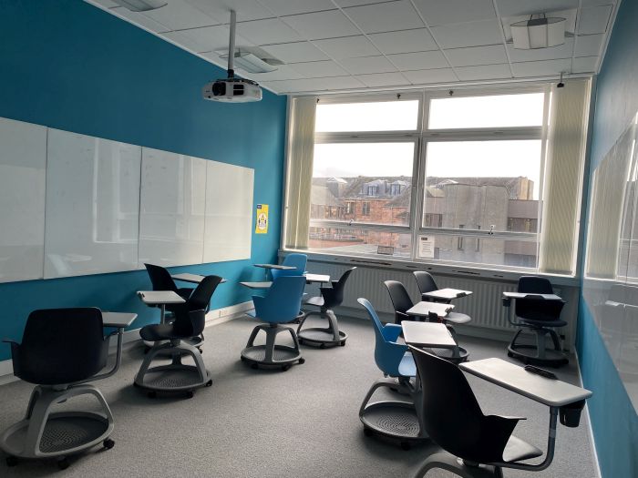 Flat floored teaching room with tablet chairs, projector, and whiteboards.