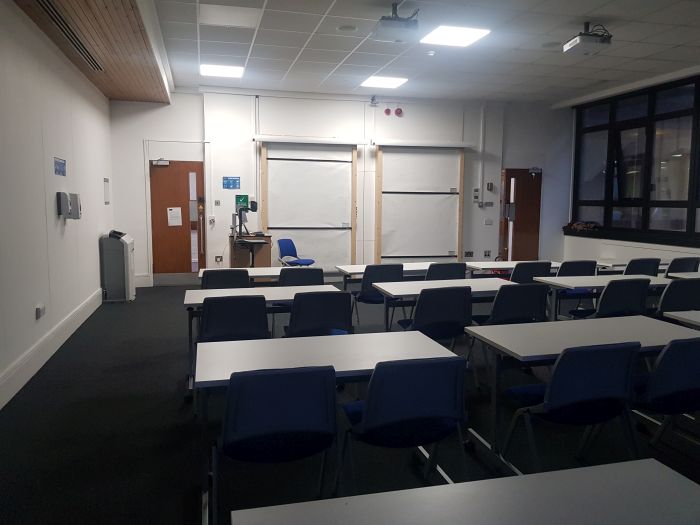 Flat floored teaching room with rows of tables and chairs, whiteboards, visualiser, and PC