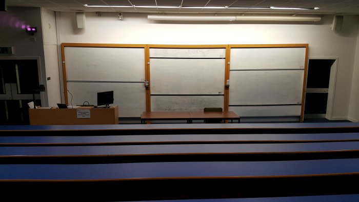 Raked lecture theatre with fixed seating, whiteboards, and PC