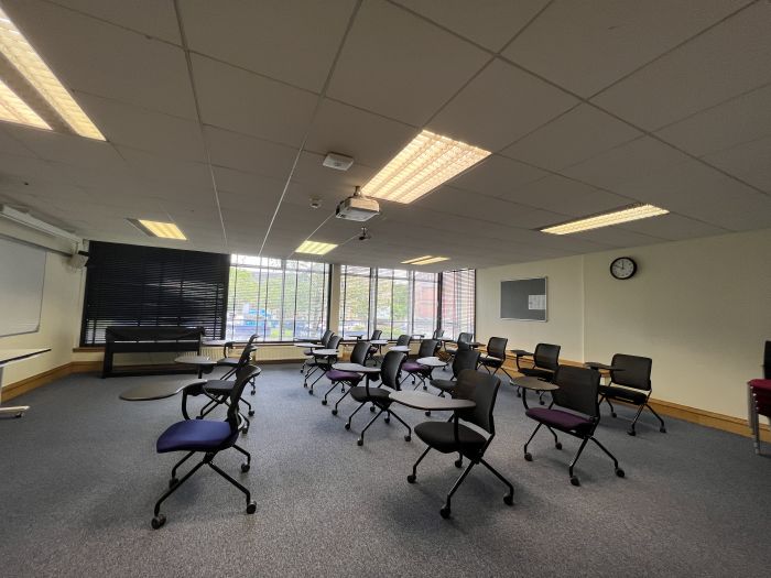 Flat floored teaching room with rows of tablet chairs, whiteboard, and projector.