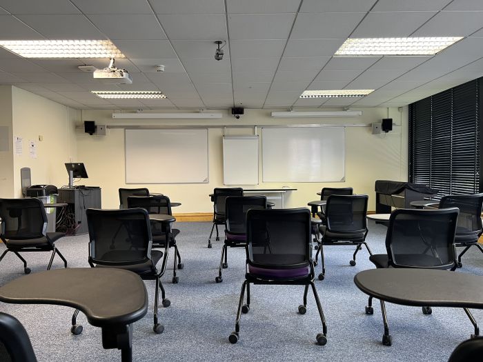Flat floored teaching room with rows of tablet chairs, whiteboards, projector, and PC.