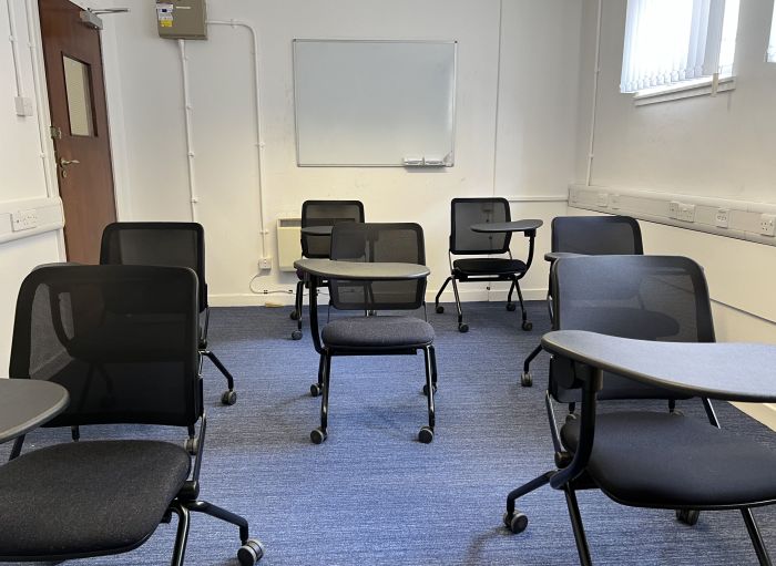 Flat floored teaching room with tables and chairs in round table set-up and video projector