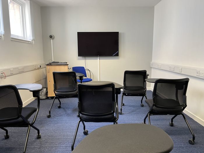 Flat floored teaching room with tables and chairs in round table set-up and whiteboard