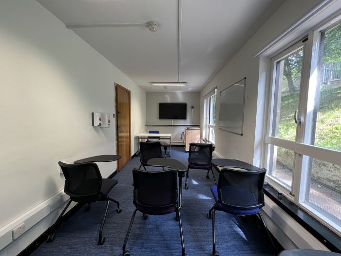 Flat floored teaching room with tablet chairs, whiteboard, video monitor, and lecturer's table and chair.