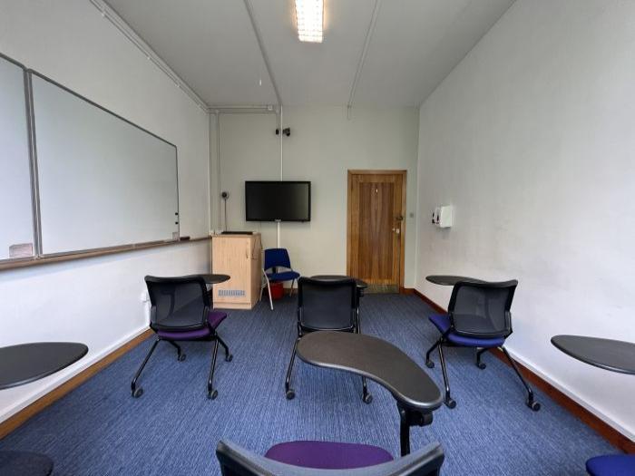 Flat floored teaching room with tablet chairs, whiteboards, video monitor, and lecturer's chair.