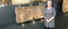 Dr Louisa Campbell in front of Summerston distance stone in The Hunterian 