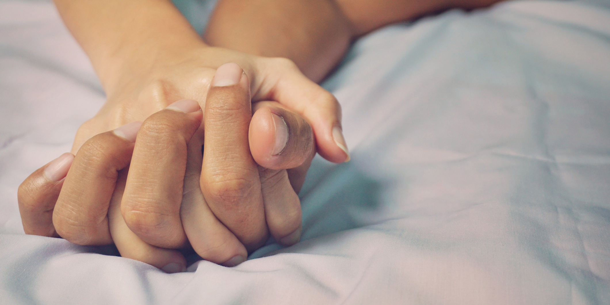 Two people holding hands in bed