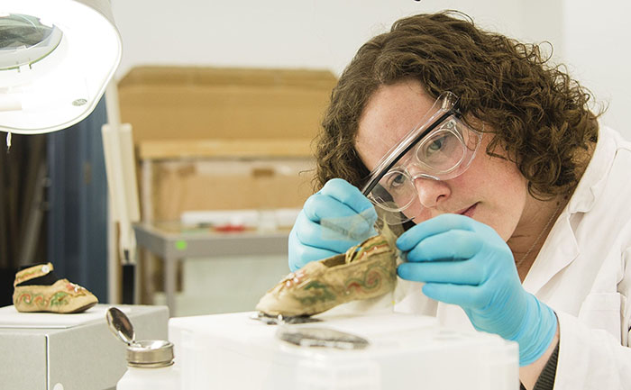 A Textile Conservation student works on a pair of shoes.