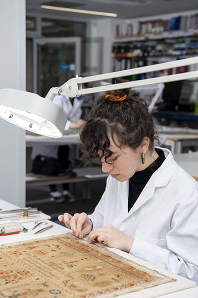 A student examines some fabric under a lamp