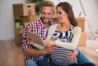 Young pregnant couple viewing tablet device, with boxes behind them, 