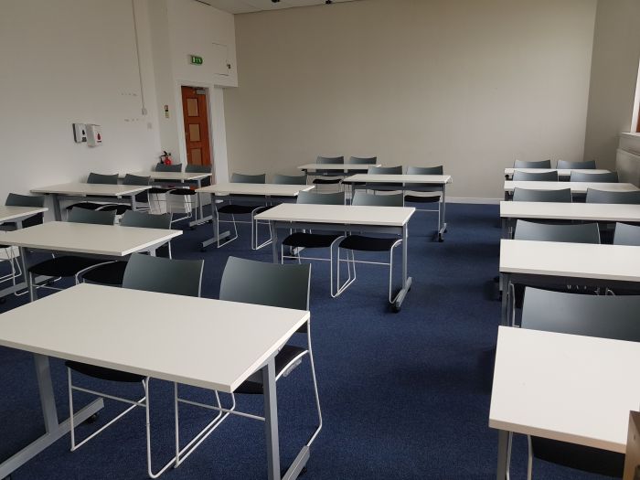 Flat floored teaching room with rows of tables and chairs.