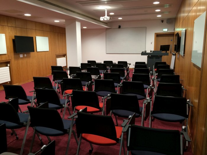 Flat floored teaching room with rows of tablet chairs, projector and screen