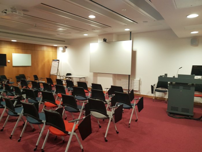 Flat floored teaching room with rows of tablet chairs, projector and screen