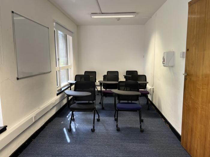 Flat floored teaching room with tablet chairs and whiteboard.