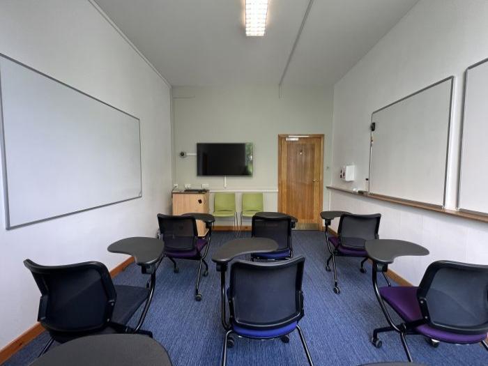 Flat floored teaching room with tablet chairs, whiteboards, video monitor, and lecturer's chair.