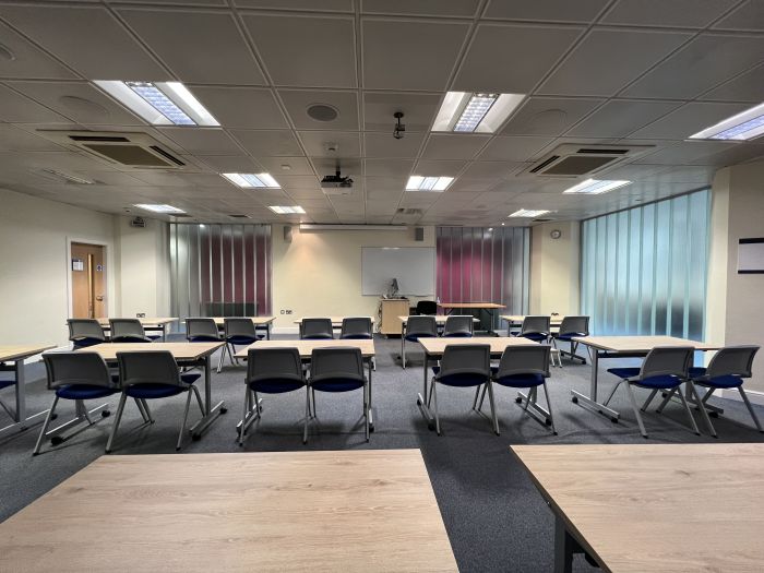 Flat floored teaching room with rows of tables and chairs, projector, PC, and whiteboard.