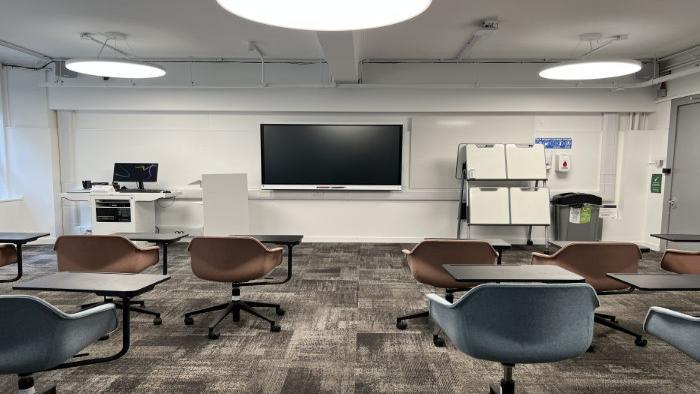 Flat floored teaching room with rows of tablet chairs, whiteboard, movable whiteboard, smart screen, handheld whiteboards, and PC.