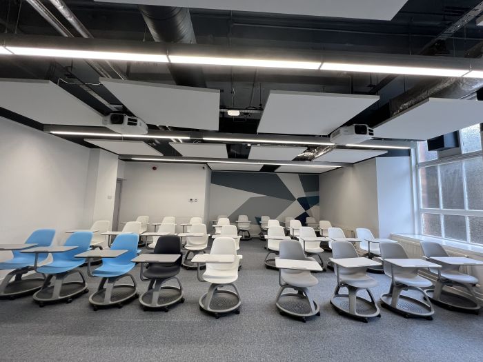 Flat floored teaching room with tablet chairs and projectors.