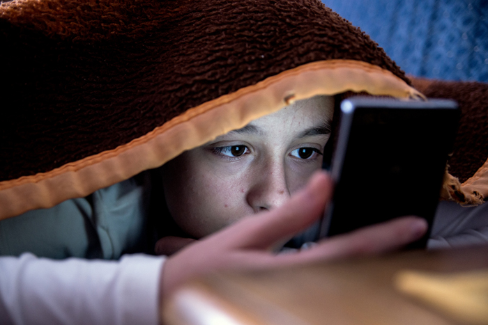 child under blanket viewing a mobile device, 700px