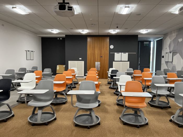 Flat floored teaching room with rows of tablet chairs, projector, and handheld whiteboards.