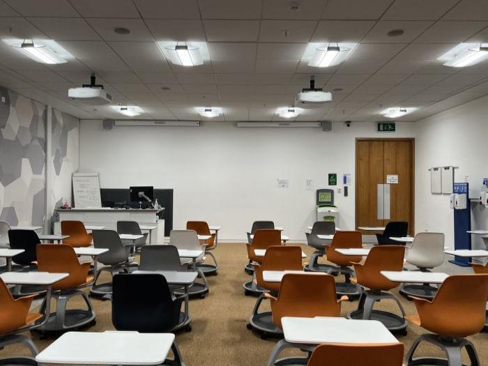 Flat floored teaching room with rows of tablet chairs, projectors, PC, and handheld whiteboards.