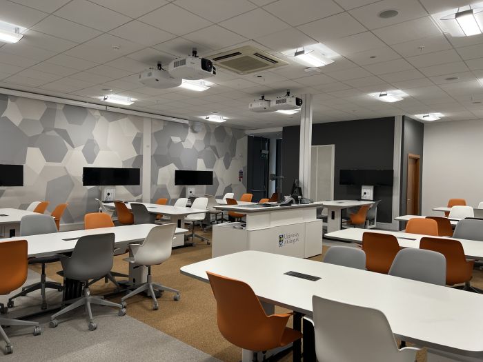 Flat floored Tech Enabled Active Learning (TEAL) room with groups of tables and chairs, each with a video monitor, as well as projectors, visualiser, PC, and lectern.