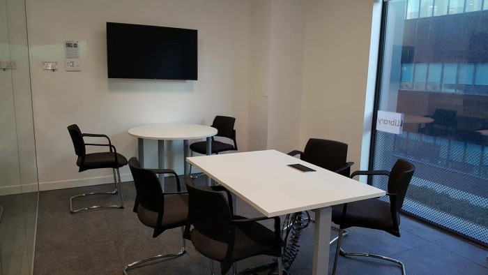 Flat floored training room with groups of tables and chairs and video monitor