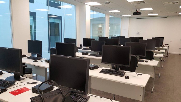 Flat floored IT lab with rows of computer desks, projector, and screen