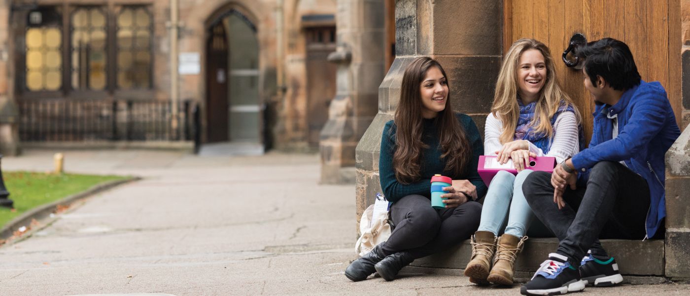 3 students sitting outside quadrangle