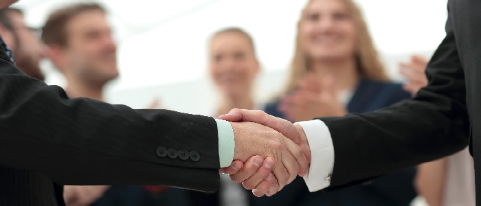 Two people shaking hands with colleagues in the background