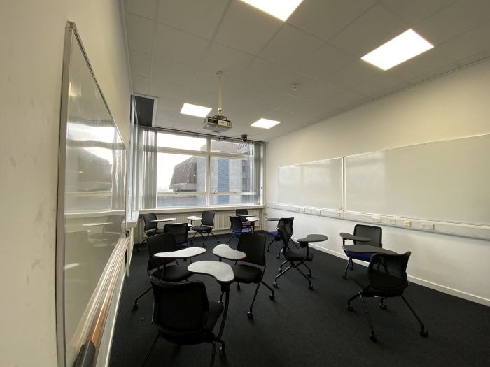 Flat floored teaching room with tablet chairs, whiteboards, and projector.