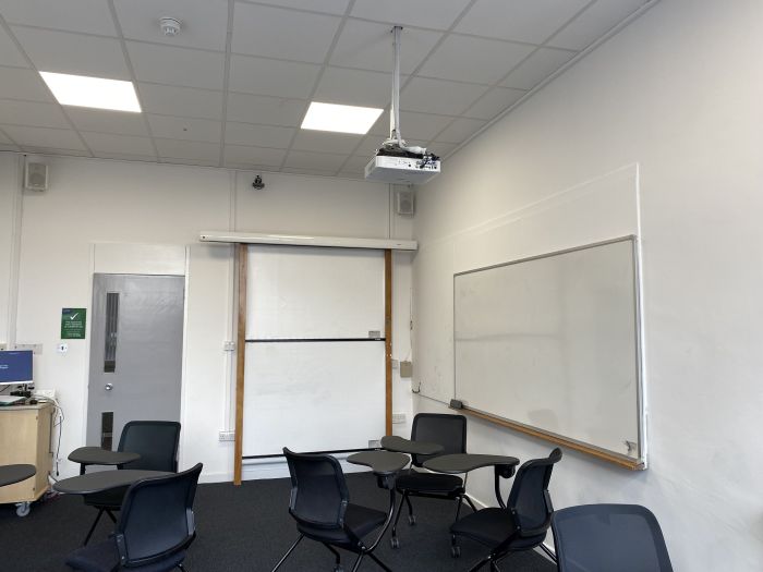 Flat floored teaching room with tablet chairs, whiteboards, PC, and projector.