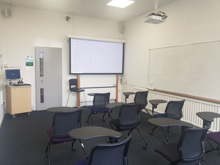 Flat floored teaching room with tablet chairs, whiteboard, PC and projector..