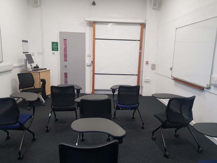 Flat floored teaching room with tablet chairs, whiteboards, and PC.