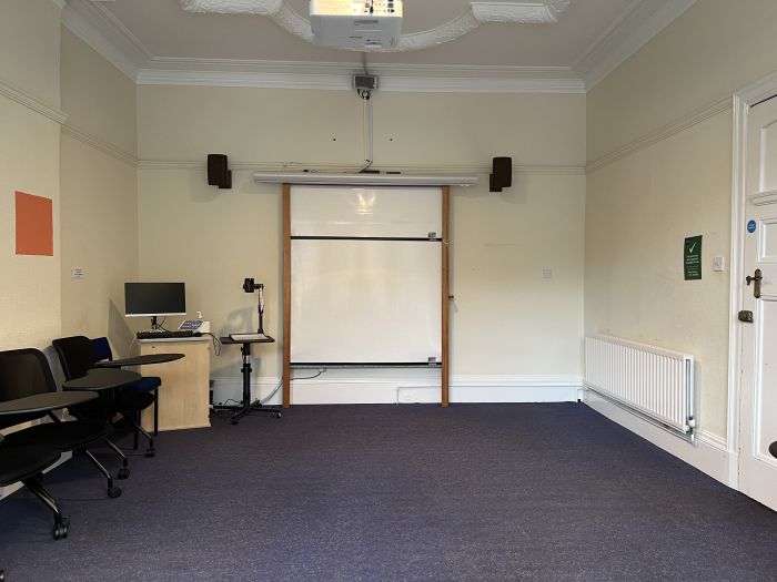 Flat floored teaching room with tablets chairs, whiteboard, visualiser, projector, and PC.
