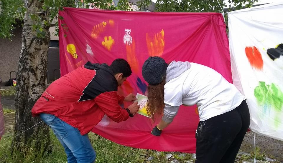 SprayPeace and a participant in the Refugee Cycle spray painting a bicycle onto a pink sheet