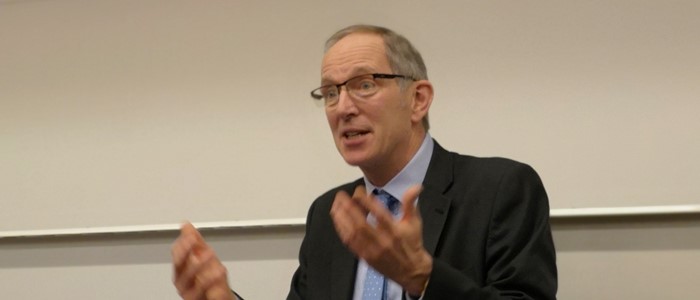 photo of a white older man in shirt and suit gesticulating while speaking