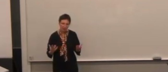 photo of a woman with dark short hair in blouse and cardigan gesticulating while speaking